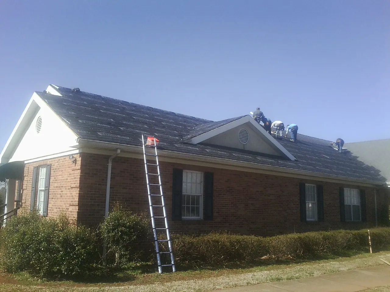 Crew tearing shingles off a brick ranch roof with a ladder set — Emergency Roof Repair work by our crew in Crucible