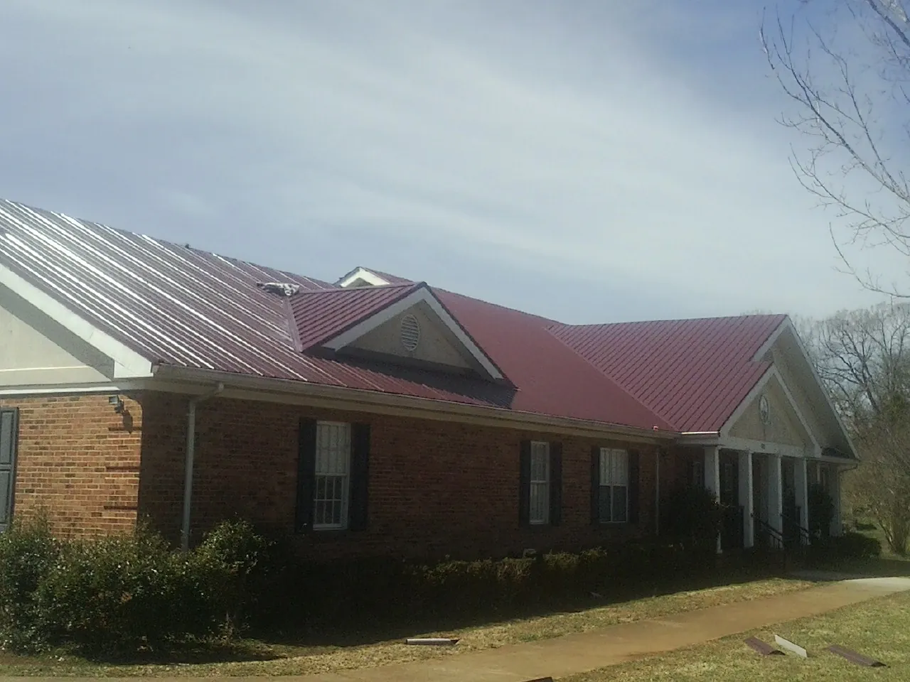 Red metal roof with gabled entries on a long brick building, from a Hail Damage Roof Repair job in Crucible