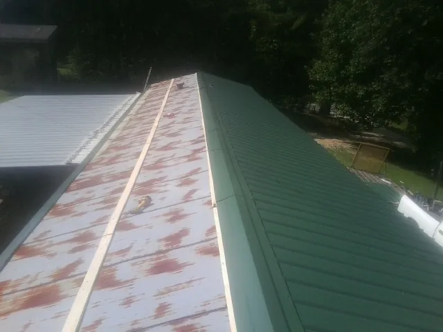 Old rusted panels beside newly installed green metal roofing — Wind Damage Roof Repair by Roofing Brothers in Crucible