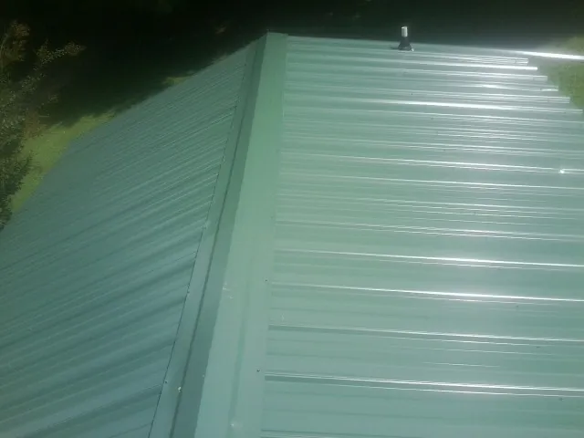 New green metal panels meeting at the ridge of a roof — Flat Roof Repair work by our crew in Crucible