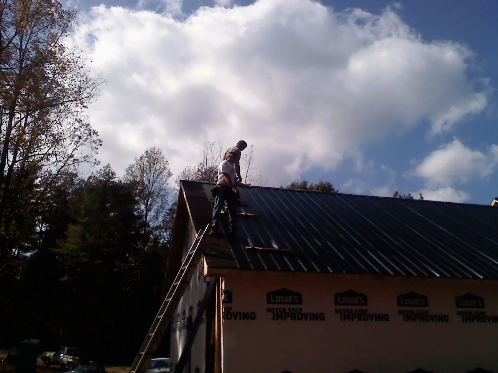 Roofer fastening dark metal panels high against a cloudy sky, from a Roof Inspection job in Crucible