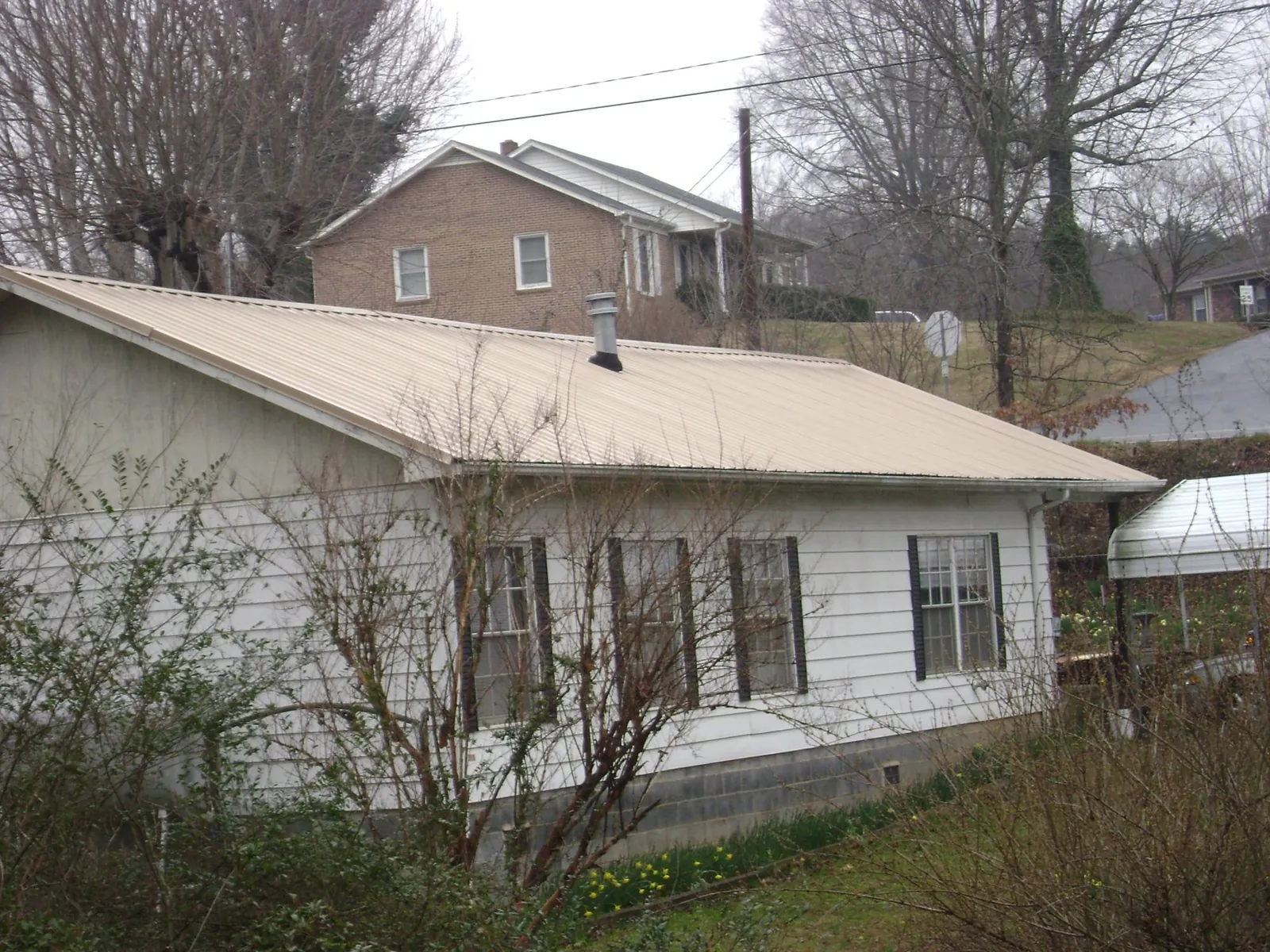 Tan metal roof on a white sided house set into a hillside — Commercial Roofing by Roofing Brothers in Crucible
