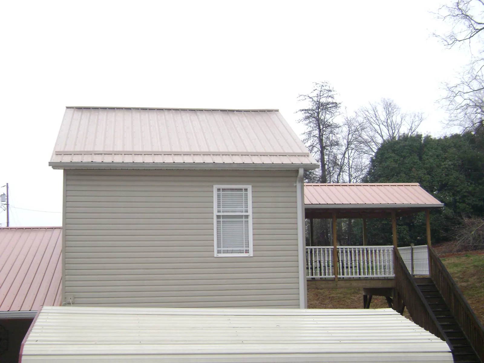 Tan metal roofs on a two story addition and attached porch, from a Roof Replacement job in Crucible
